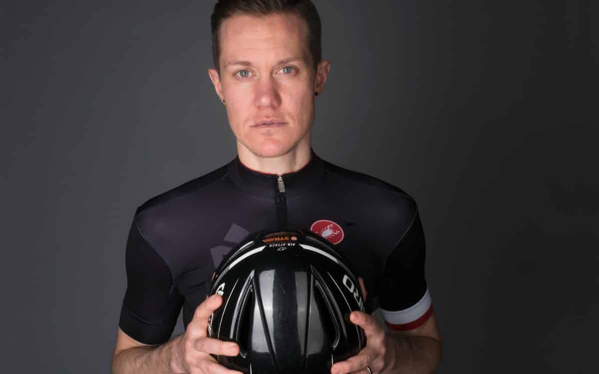 Chris Mosier holding bicycle helmet in a black background